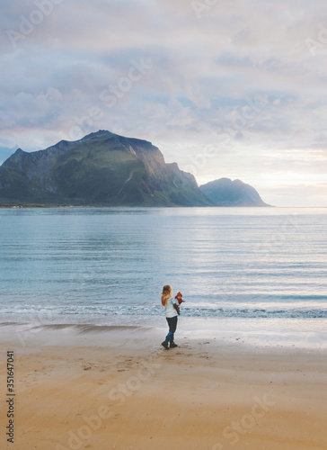 Mother walking with baby on sandy beach family travel in Norway summer vacations outdoor woman with child enjoying sunset ocean and mountains view