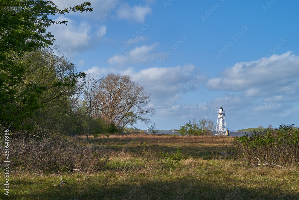 scenic white lighthouse on the island Elsflether Sand in the river Weser seen behind natural greenery on a sunny day with vivid blue sky and white clouds scenic white lighthouse on the island Elsflether Sand in the river Weser seen behind natural greenery on a sunny day with vivid blue sky and white clouds