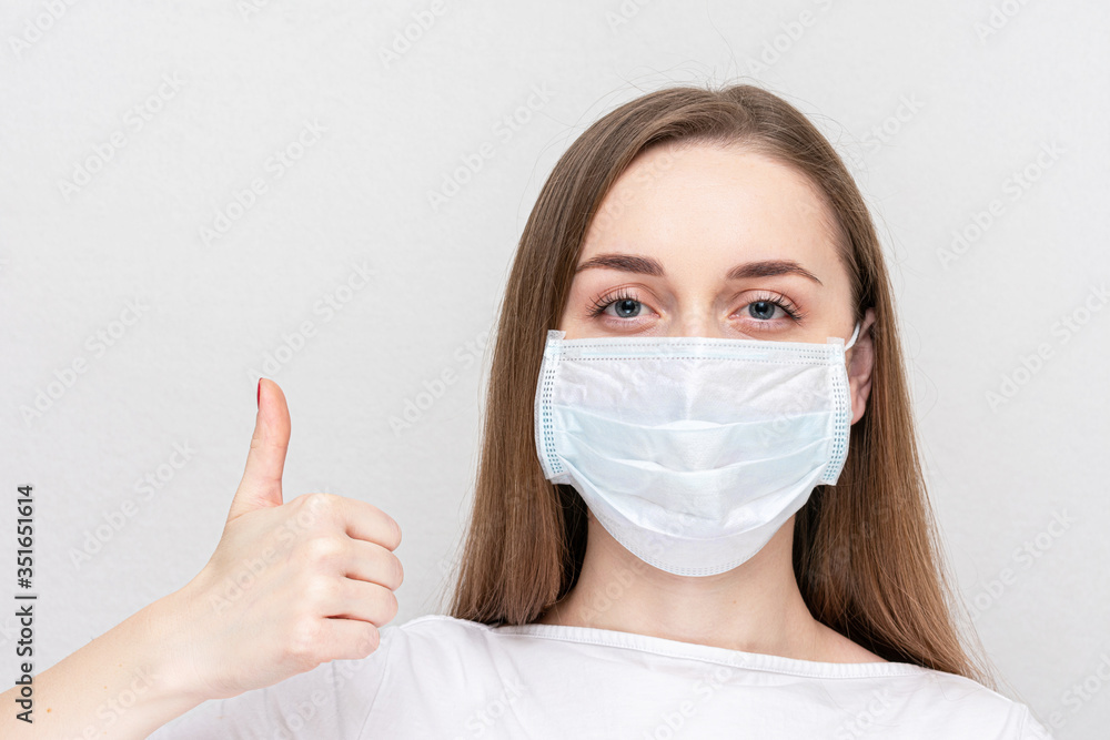 Woman wearing medical mask shows thumb up, white background Woman wearing medical mask shows thumb up, white background
