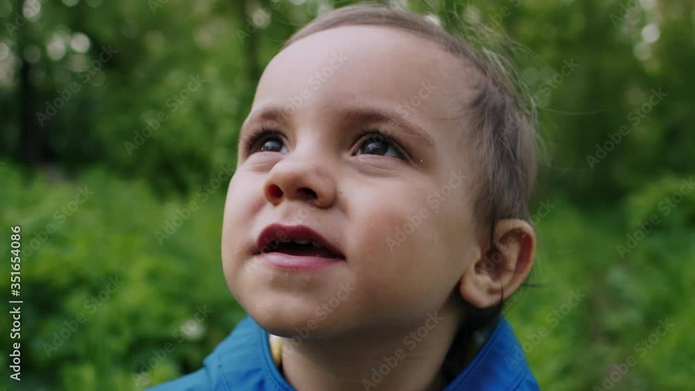 Portrait of adorable baby boy smiling and laughing on green forest background. Cute kid in blue raincoat. Family, love, child concept. Portrait of adorable baby boy smiling and laughing on green forest background. Cute kid in blue raincoat. Family, love, child concept.