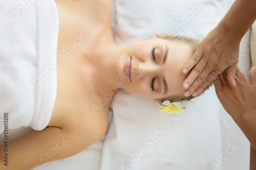 Beauty woman having massage on face  head on spa bed at spa salon with smile face. Massage therapist massage customer face  rejuvenating look younger facial skin. spa treatment. Comfortable  top view