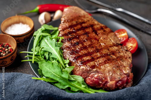 delicious grilled beef steak with spices and herbs on a black plate on a stone background