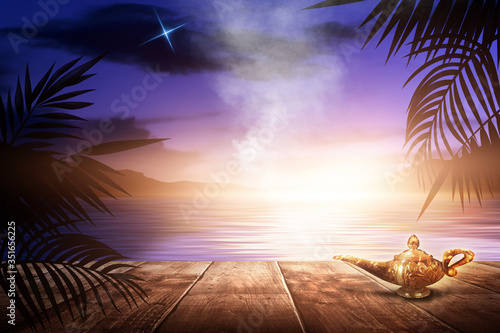 Aladin's lamp on the background of a sea evening landscape with sunset. Palm tree branches, silhouettes, sunlight. Wooden table. Night view, open-air seascape. 3D illustration photo