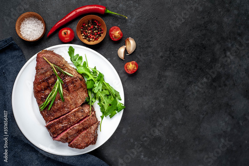 Grilled beef steak with spices, tomatoes and herbs on a white plate on a stone background with copy space for your text.