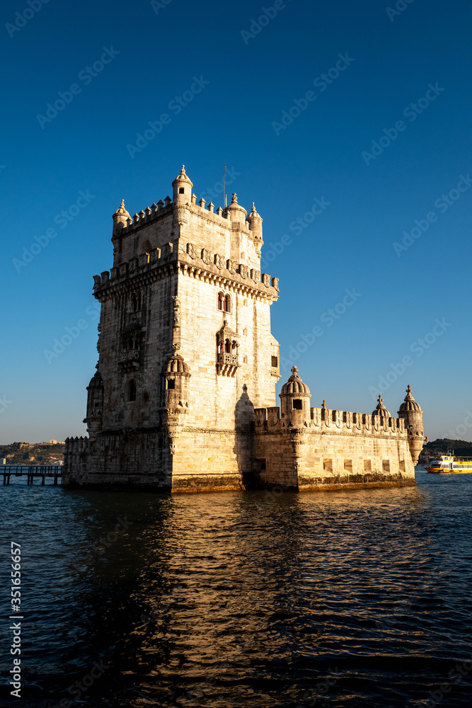 The tower of Belem in Lisbon illuminated by the setting sun with a boat passing in the background.