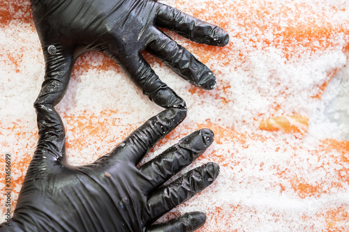 Master shusi with black hygienic gloves cleaning and preparing a huge fresh salmon.Salting the fish in a bowl. Kitchen and food concept photo