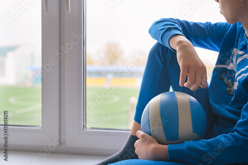 The boy sits by the window, wanting to go out and play with the ball