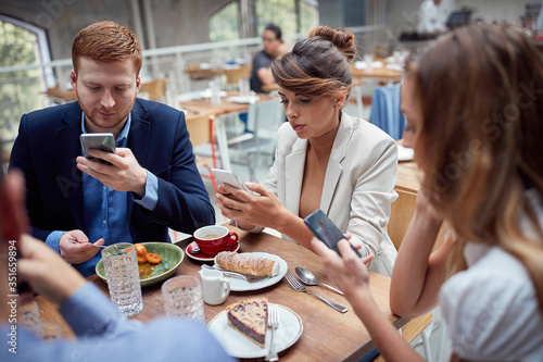 young people having unsocial lunch in restaurant, using their cell phones and not talking to each other. social issues, victims of modern technology photo