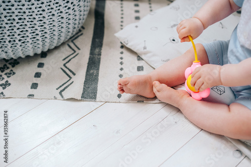 A small child sits on the floor on the carpet and plays a colored rattle