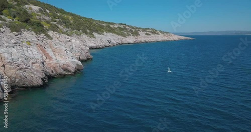 Forward drone shot next to a rocky shore in the aegean sea crossing paths with a seagull. Shot in 4K photo