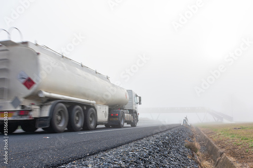 Tank truck in motion driving on a highway with dense fog
