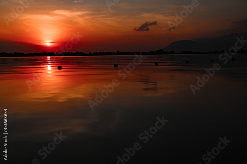 Cinematic red sunset sky reflected on the still waters of the Mekong River during the hot and humid summer season in Cambodia
