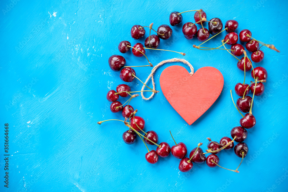 Obraz premium circle of red heart and cherry berries with stem on blue background and water drops top view.Beautiful food circle Frame of red ripe cherries. Arrangement of fresh berries. Flat lay.Copy space