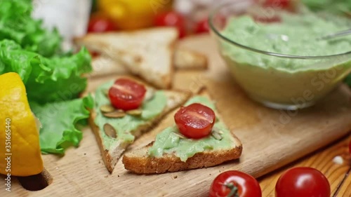 Toasts with avocado and guacamole with various fresh summer products on the table in slow motion. Cooking a delicious healthy vegetarian breakfast. Healthy eating and healthy lifestyle.