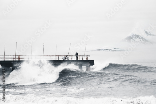 A cyclist watches from the pier the huge sea waves in a storm.