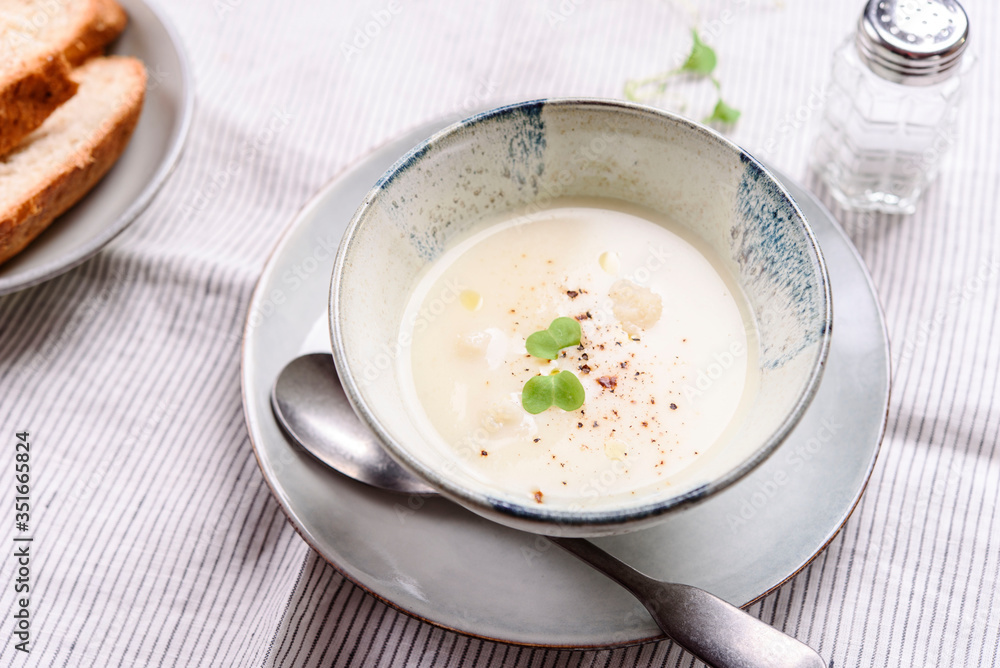 Cauliflower and Potato Cream Soup served with herbs and pepper on white linen striped tablecloth. Selective focus Cauliflower and Potato Cream Soup served with herbs and pepper on white linen striped tablecloth. Selective focus