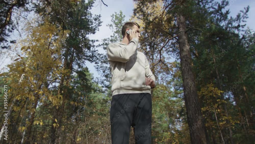 Healthy man in comfortable clothes waiting in forest at autumn sunny morning and having phone call. Low angle 4K 360 degree tracking arc shot. Healthy man in comfortable clothes waiting in forest at autumn sunny morning and having phone call. Low angle 4K 360 degree tracking arc shot.