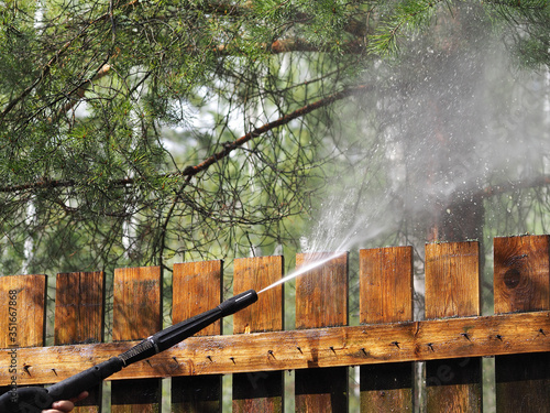 Gardening in the spring. Seasonal handling and cleaning of wooden fence from dirt and bacteria during corona virus covid-19 with high-pressure washing equipment containing disinfectant photo