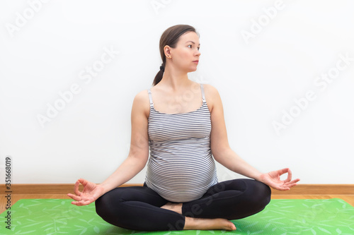 Pregnant woman sitting in lotus position and practising yoga at home