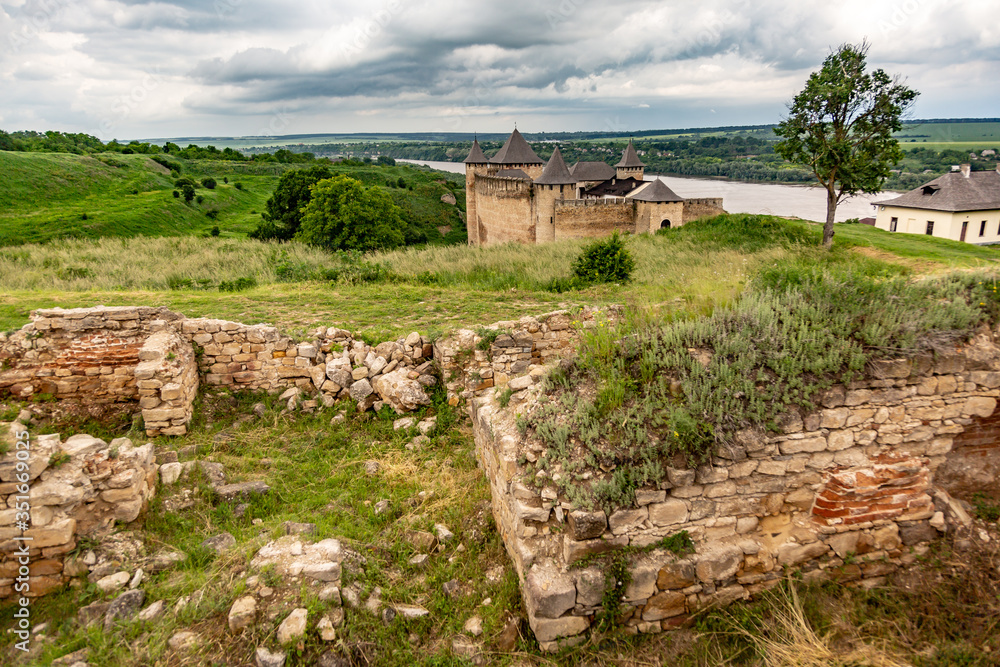 Khotyn Fortress castle in Ukraine, river on a background of dark clouds on a cloudy windy day in summer. Brick ruins in the foreground. Horizontal orientation.