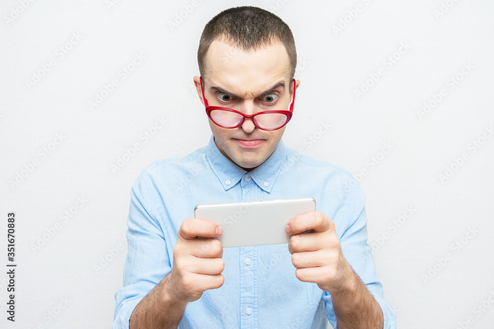 Young nerd is focused on playing games on a mobile phone, guy red glasses, portrait, white background Young nerd is focused on playing games on a mobile phone, guy red glasses, portrait, white background