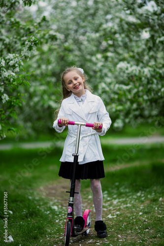 Cute little girl riding a scooter Child on scooter in park. Outdoor activity for children on safe blooming park.