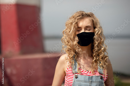 Obraz na plátně A girl with curly hair and an antiviral mask walks in sunny weather on the stree