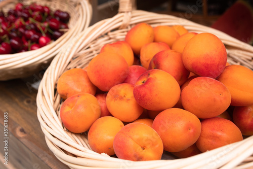 A basket with freshly picked apricots and cherries in the background