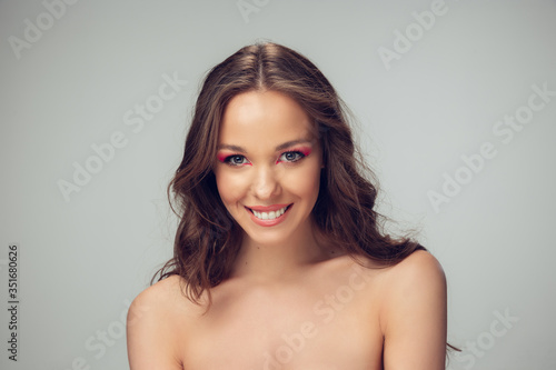 Close up of beautiful young woman with long healthy curly hair and bright make up isolated on grey studio backgroud. Beauty and fashion, hair and skin care, treatment concept. Well-kept healthful girl