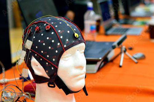 The electroencephalogram (EEG) head cap with flat metal discs (electrodes) attached to a head model with laptops blurred at background. Concept of brain science and Artificial Intelligence (AI) . photo