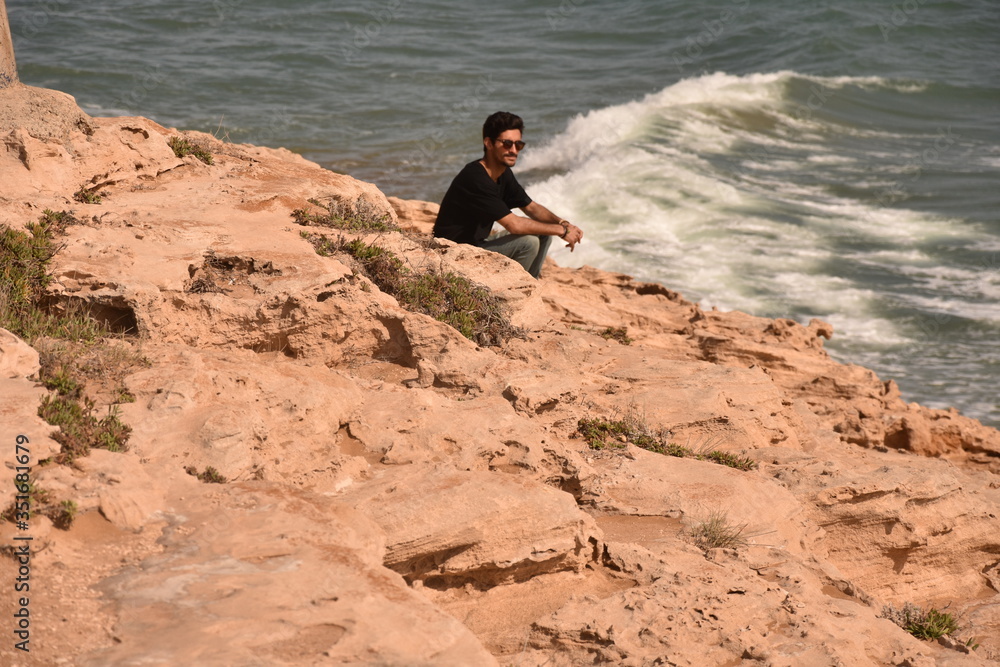 Young man sitting next to a beautiful beach. Boy with a black t-shirt looking to the paradise, or maybe a desert. Young man sitting next to a beautiful beach. Boy with a black t-shirt looking to the paradise, or maybe a desert.