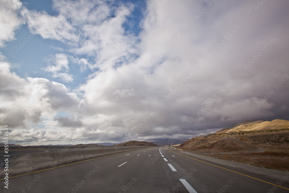 Asphalt road and bright blue sky with fluffy clouds . Empty desert asphalt road from low angle with mountains and clouds on background. road, red desert landscape . Open road with blue clouds .