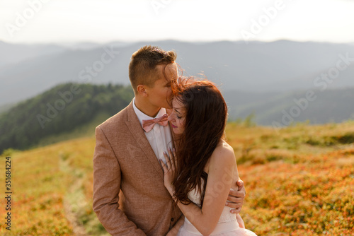 The bride and groom hug and tenderly with each other. Sunset. Wedding photo on a background of autumn mountains. A strong wind inflates hair and dress. Close-up. © wolfhound911