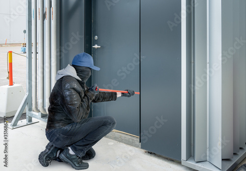 burglar with a mask and crowbar breaks into a building