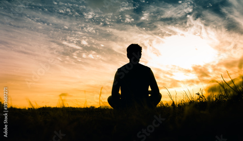 Konstfotografi Man sitting on grass field watching the sunset