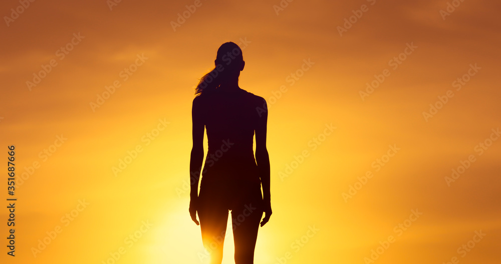 Silhouette of female standing facing sunset. 