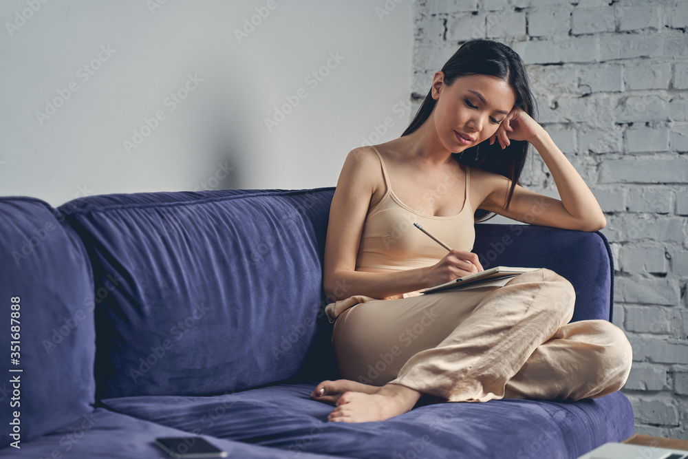 Fototapeta premium Beautiful young woman writing in notebook at home