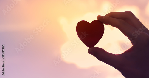 Hand holding heart against sunset sky. Love concept. 