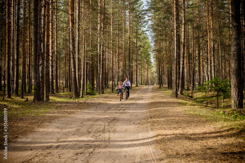 mother and little daughter riding bikes in summer forest.Family on a bike ride together outdoors on a sunny day.Mom and daugther having fun together riding bicycle together, in green park or forest.