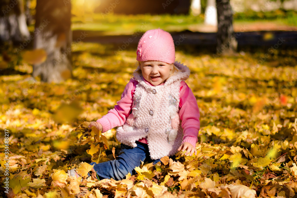 Child in yellow autumn leaves rejoices in autumn. Autumn orange leaves are falling on baby girl, sunny weather. Child in yellow autumn leaves rejoices in autumn. Autumn orange leaves are falling on baby girl, sunny weather.