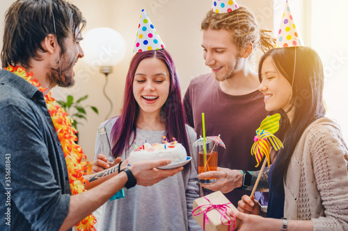Happy young girl celebrating birthday among friends while standing in room at home