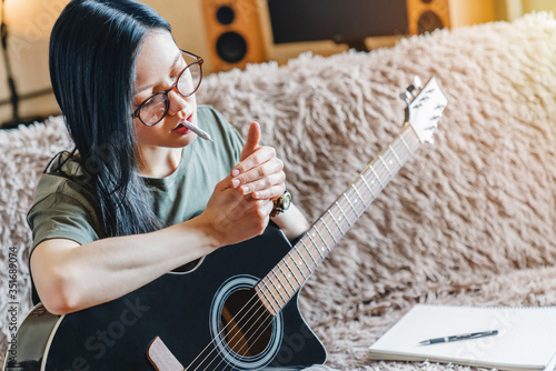 Young girl lighting marijuana joint while holding guitar at home photo