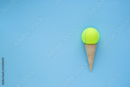 Yellow tennis ball in ice cream waffle cone , summer sport concept, on blue background . Space for text. 
