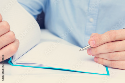 Man with pen writes in a notebook, close-up