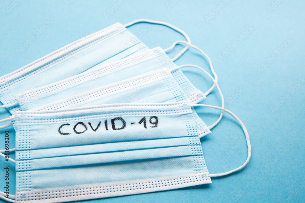 Top view several medical face masks with note COVID-19 on a blue background. Coronavirus infection prevention concept Top view several medical face masks with note COVID-19 on a blue background. Coronavirus infection prevention concept