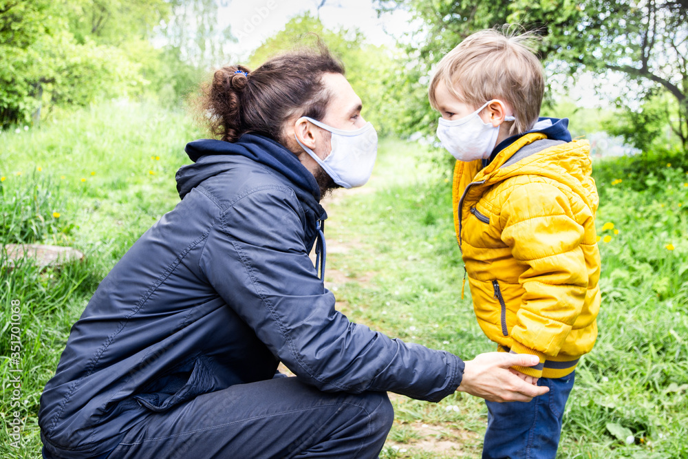 Father and little son wear face masks outdoor. The father holds the child by the hand. End of quarantine and mandatory wearing of masks. Family protection during the coronavirus pandemic concept.