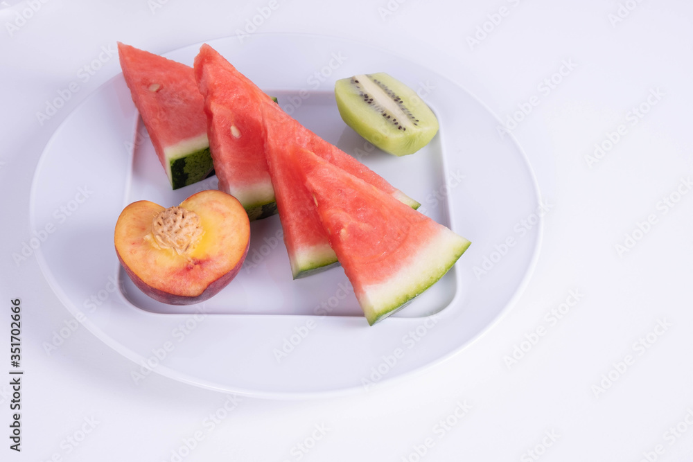 four slices of watermelon, peach and kiwi on a plate on a white background four slices of watermelon, peach and kiwi on a plate on a white background