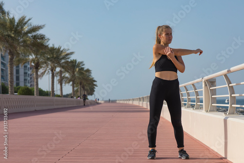 Portrait of a young woman stretching hands isolated. Portrait of a fitness woman doing warm up exercises outdoors. Attractive woman stretching. Young fit woman athlete stretching before run. Dubai 