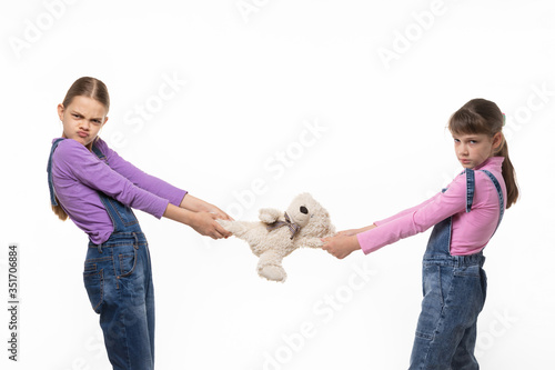 Two disgruntled sisters share a toy on a white background photo