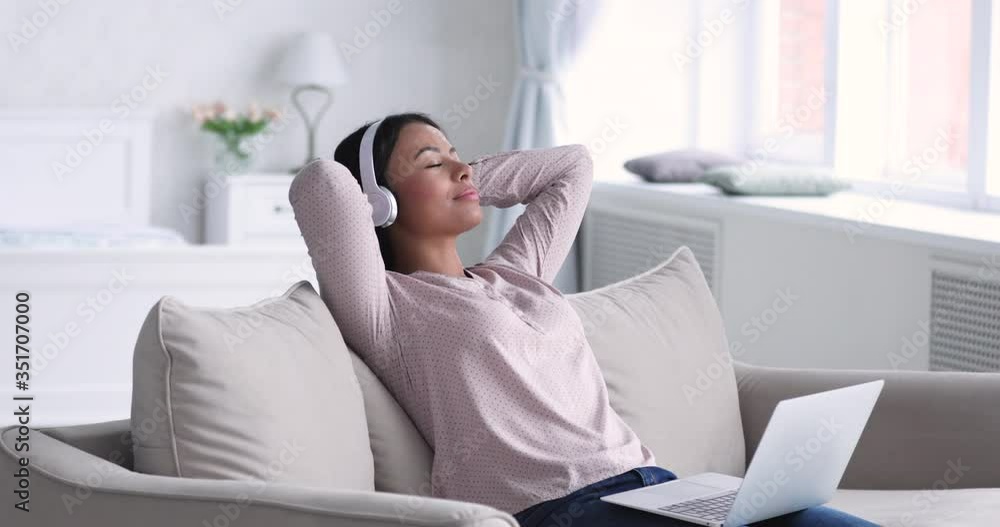Peaceful young african american woman holding computer on lap, relaxing with favorite slow music in earphones. Carefree happy biracial female freelance worker enjoying break pause time alone at home. Peaceful young african american woman holding computer on lap, relaxing with favorite slow music in earphones. Carefree happy biracial female freelance worker enjoying break pause time alone at home.